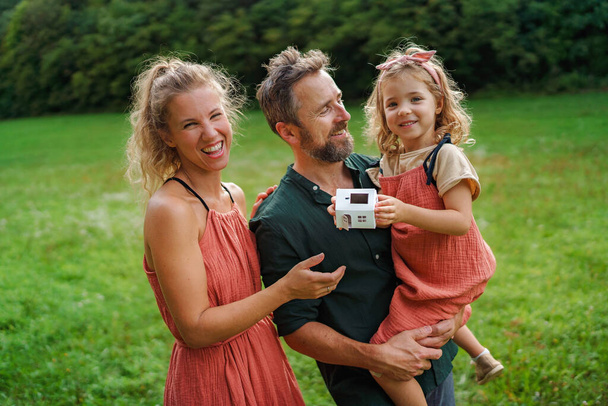Bambina con i suoi genitori in possesso di modello di carta di casa con i pannelli solari. Energia alternativa, risparmio di risorse e concetto di stile di vita sostenibile. - Foto, immagini