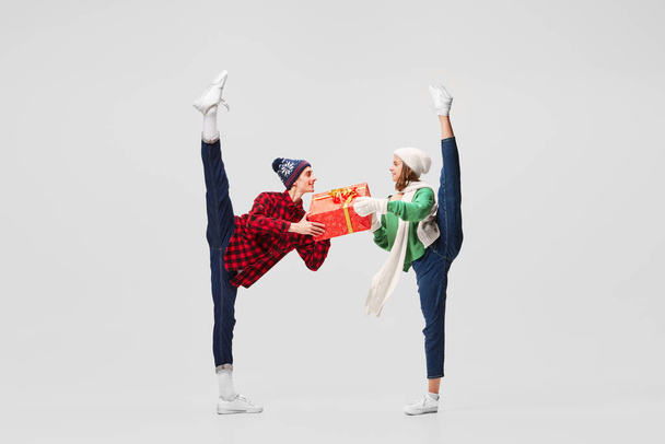 Stretching. Emotional young people, ballet dancers in warm clothes in action, motion with bright festive gift boxes on gray background. Merry Christmas, New year, holidays, 2023, party concept - Valokuva, kuva