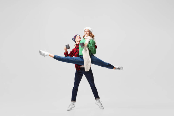 Hot drinks. Cute young couple of ballet dancers in warm winter sportswear drinking tea or mulled wine isolated on gray background. Retro, vintage, dance, holidays, family concept. Copy space for ad - Φωτογραφία, εικόνα