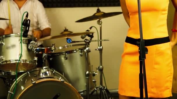Sänger bereitet sich auf seinen Auftritt vor. Frau mit Mikrofon in leuchtend orangefarbenem Kleid bereitet sich auf das Singen vor. Der Mann spielt Schlagzeug. Musikstudio mit Mikrofonen und Schlagzeug. Musikshow auf der Bühne. - Filmmaterial, Video