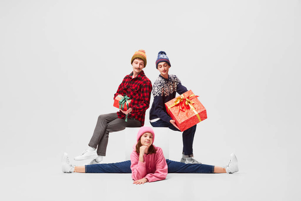 Girls choice. Emotional young people, ballet dancers in warm clothes sitting with bright festive gift boxes on gray background. Merry Christmas, New year, holidays, 2023, party concept - Fotó, kép