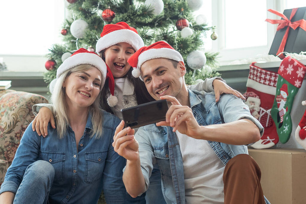 Karácsonyi család. Boldogság. Apa, anya és lánya portréja otthon, a karácsonyfa mellett, mind mosolyognak.. - Fotó, kép