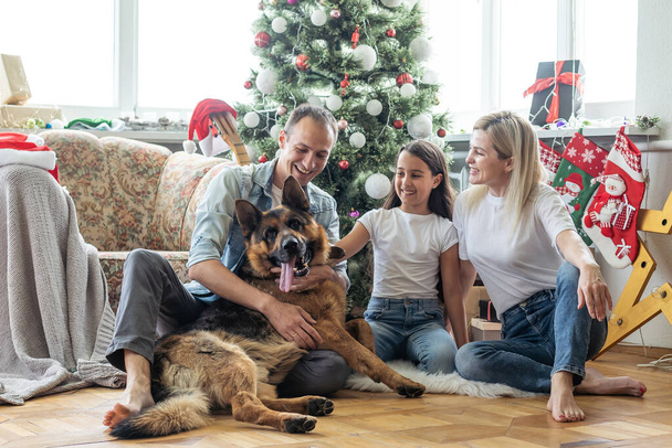 Nadšená dívka a její rodina sedí na podlaze u vánočního stromku a usmívají se. rodina během Vánoc. - Fotografie, Obrázek