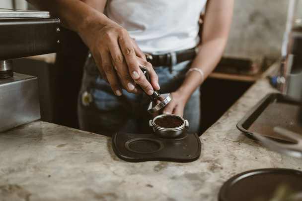 Barista using a tamper to press ground coffee into a portafilter. Coffee maker concept - Photo, Image