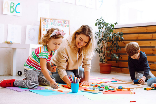 Sorrindo psicólogo feminino jogar e testar crianças, fazer artesanato, brinquedos artesanais e artes no centro de desenvolvimento infantil para pré-escolares. TDAH, transtorno do déficit de atenção, autismo infantil e cuidados infantis - Foto, Imagem