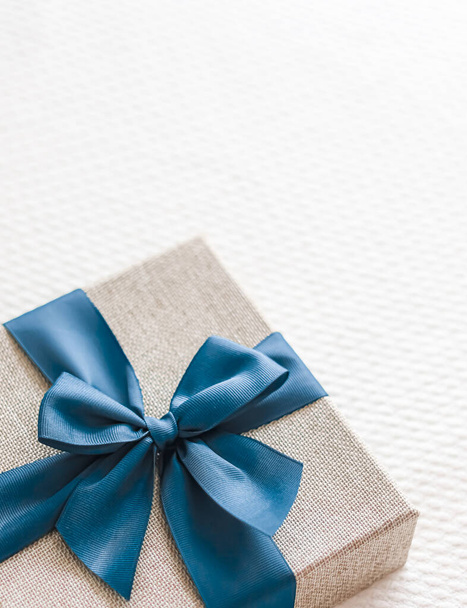 Holiday present and luxury online shopping delivery, wrapped linen gift box with blue ribbon on bed in bedroom, chic countryside style, close-up - Foto, Imagen