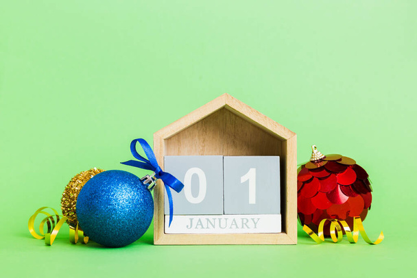 1 january. Christmas composition on colored background with a wooden calendar, with a gift box, toys, bauble copy space. - 写真・画像