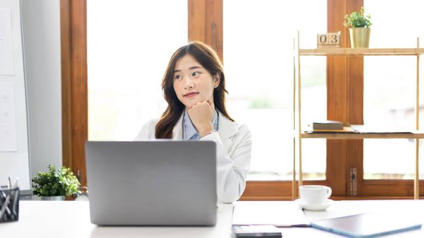 Laptopot használó üzletasszony, az irodában dolgozó ázsiai nő, pénztáros vagy könyvelő az asztalon dolgozó dokumentumokkal és berendezésekkel, számítógépek használata pénzügyi tranzakciókhoz. - Fotó, kép