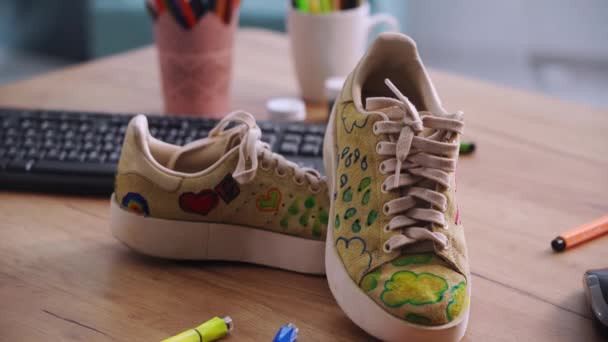 λογική κατανάλωση πραγμάτων, επώνυμα sneakers με μοντέρνο print stand στο τραπέζι με χρώματα και μαρκαδόρους, close-up - Πλάνα, βίντεο