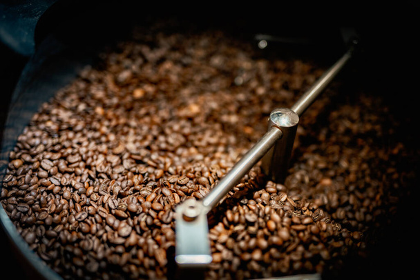 Cierre la espátula de la máquina con granos de café marrones arabica cerca de equipo especial. Concepto de fábrica. - Foto, imagen