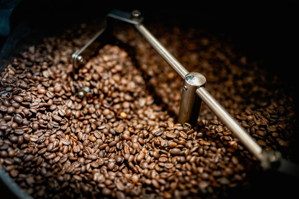 Close up machine spatula with brown arabica coffee beans near special equipment. Factory concept. - 写真・画像