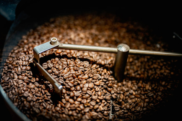 Close up machine spatula with brown arabica coffee beans near special equipment. Factory concept. - Фото, зображення