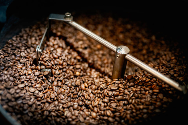 Close up machine spatula with brown arabica coffee beans near special equipment. Factory concept. - Zdjęcie, obraz