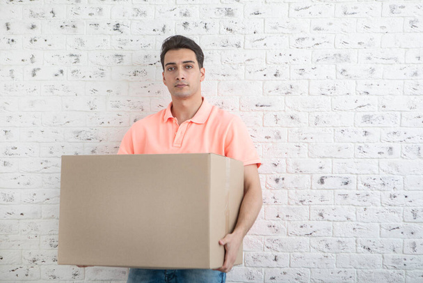 Beau homme portant une lourde boîte devant le fond du mur de briques blanches - Photo, image