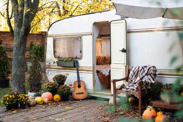 Мобільний домашній фургон з терасою на заході сонця восени, мобільний будинок, оранжеве опале листя. осінній декор, гарбузи
. - Фото, зображення