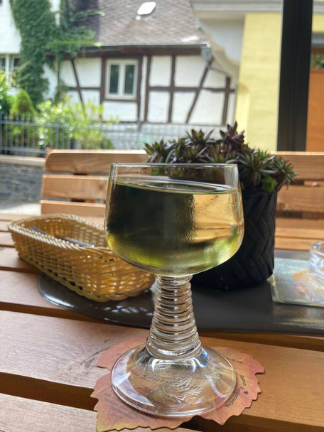 bílé víno v retro německé vinné sklenici na dřevěném stole s bokeh pozadím zpola roubeného domu - Fotografie, Obrázek