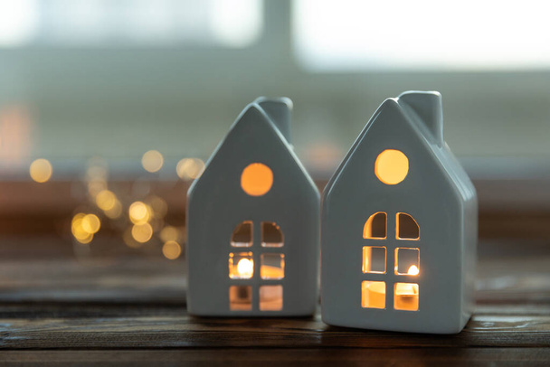 Small candlestick Christmas houses with burning candle inside on blurred window background. Real estate, holiday, Christmas, miniature.Christmas cozy interior decor. - Φωτογραφία, εικόνα