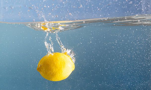 Свежий лимон, пропитанный глубокими брызгами голубой воды. Вода из голубого бассейна и фруктовое движение. Креативная концепция летнего питания - Фото, изображение