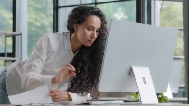 Jeune femme hispanique attrayante gestionnaire professionnel développeur travaillant dans un bureau moderne axée femme d'affaires vérifier les informations électroniques sur ordinateur à l'aide de documents papier de recherche de données de vente - Séquence, vidéo