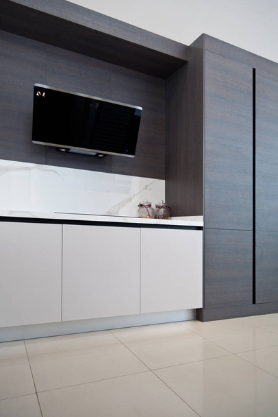 Modern szürke fehér lakk fa konyhaszekrény berendezés és fekete elektromos tűzhely és motorháztető fehér gránit pult otthon - Fotó, kép