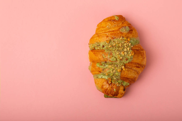 Croissant fresco sobre fondo rosa. Croissant casero delicioso con corteza de pistacho. Lugar para el texto. Lugar para copiar. Puesta plana - Foto, imagen