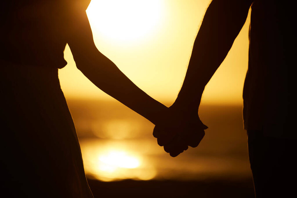 日没時にビーチで夫婦の手。カップルのシルエットは、ビーチで手を握っている。カップルの休日の海で結合します。海による休暇における関係のカップル. - 写真・画像