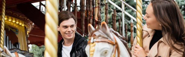 vidám fiatalember nézi barátnő lovaglás körhinta ló vidámpark, banner - Fotó, kép