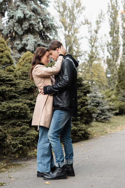 full length of young woman in beige trench coat hugging boyfriend in black jacket - Fotografie, Obrázek