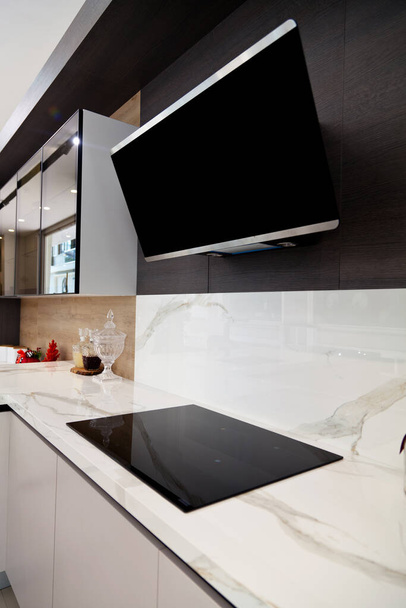 Modern gray white lacquer wood kitchen cabinet equipment and black electric stove and hood on white granite countertop in home - Foto, Imagem