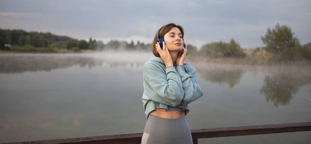 Portré gyönyörű fitt nő visel fejhallgató és zenét hallgatni kocogás után a természetben. Pihenő- és relaxációs koncepció - Fotó, kép