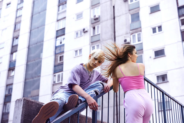 Teenagers sit in urban exterior surrounded by the buildings. - 写真・画像