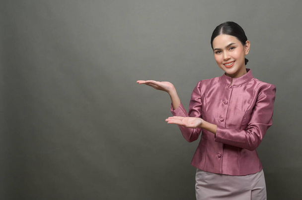 Młoda Azjatka ubrana w tajski tradycyjny materiał na szarym tle - Zdjęcie, obraz