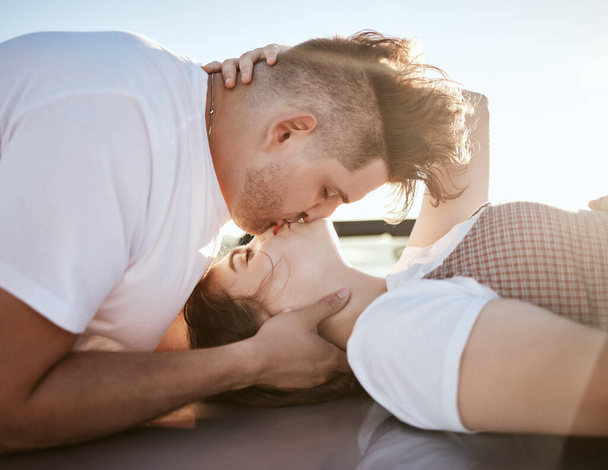 Love, intimacy and couple kiss and relax together outdoor, touching lips and having fun. Romance, flirting and affection by young man and woman showing desire and passion while kissing outside. - Photo, Image