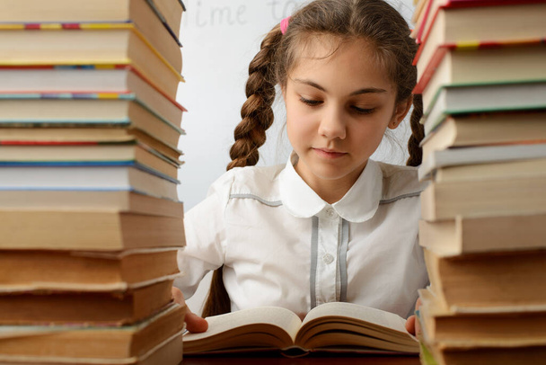 Schulmädchen zwischen Bücherstapeln. Kleines Mädchen beim Lesen eines Buches. Konzept von Bildung, Lesen, Lernen - Foto, Bild