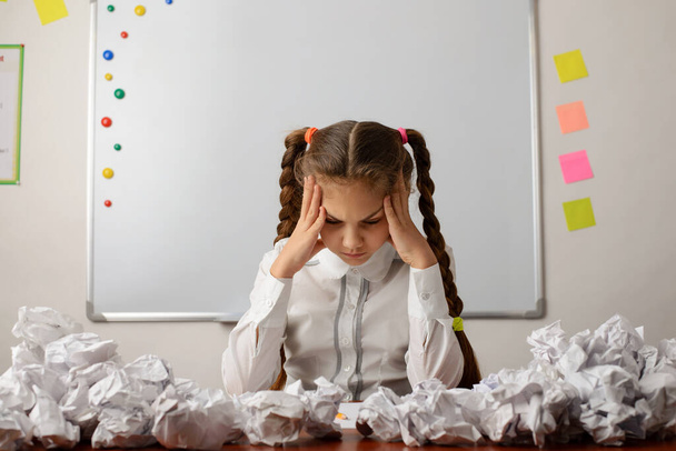 Concept of brainstorming, thinking hard, failure, difficult decision, doing difficult task. Little girl in the classroom sitting around many crumpled papers - Photo, Image
