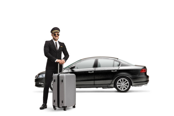 Full length profile shot of a chauffeur standing in front of a black car with a suitcase isolated on white background - Foto, immagini