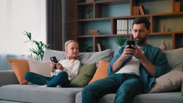 焦点を当てた父親の親と子供の娘は、ソファの上に座っているスマートフォンのデバイスは、オンラインアップロードモバイルアプリをチャット見てガジェットから中毒多様な家族世代現代の技術の過剰使用 - 映像、動画