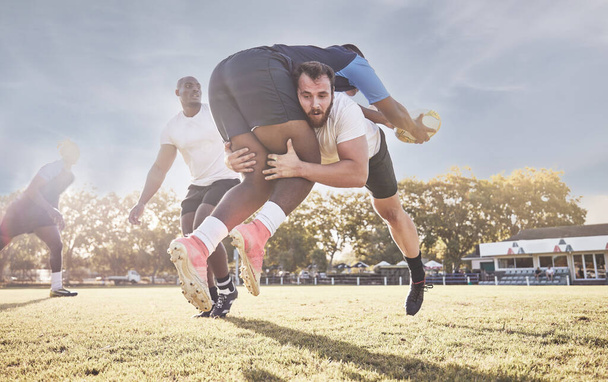 Caucasian rugby player attempting to tackle an opponent during a rugby match outside on the field. Young athletic man tackling an opponent in an attempt to stop him from scoring. Last line of defense. - Fotografie, Obrázek