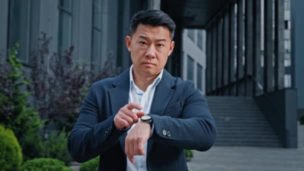 Enojado preocupado 40s asiático hombre de negocios frustrado jefe gerente CEO esperando reunión al aire libre en la ciudad nerviosa molestia frustrado señalando en reloj de pulsera tarde tiempo retraso plazo puntual espera - Imágenes, Vídeo