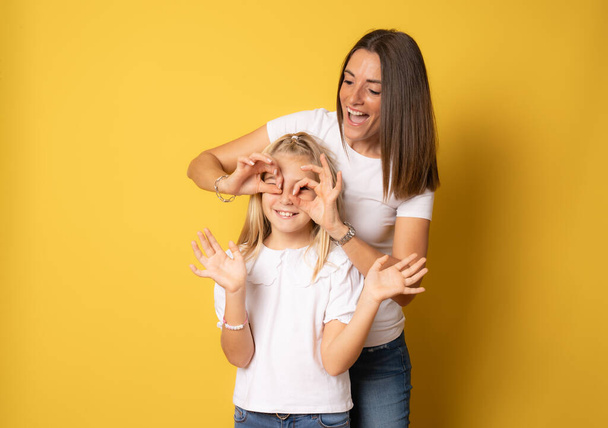 Hermosa madre e hija sonriendo felices divirtiéndose juntas sobre un fondo amarillo aislado. - Foto, Imagen