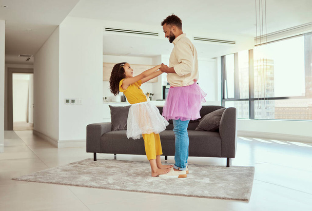 Full length mixed race single father dancing with adorable daughter in living room at home. Cute little hispanic girl wearing tutus with single parent and bonding in lounge. Man and child together. - Фото, изображение