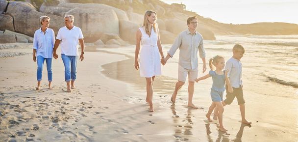Monen sukupolven perhe pitää toisiaan kädestä ja kävelee rannalla yhdessä. Valkoihoinen perhe, jossa kaksi lasta, kaksi vanhempaa ja isovanhemmat nauttivat kesälomasta. - Valokuva, kuva