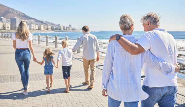 Rear view of a senior couple strolling on a seaside promenade while their children and grandchildren walks ahead - Photo, Image
