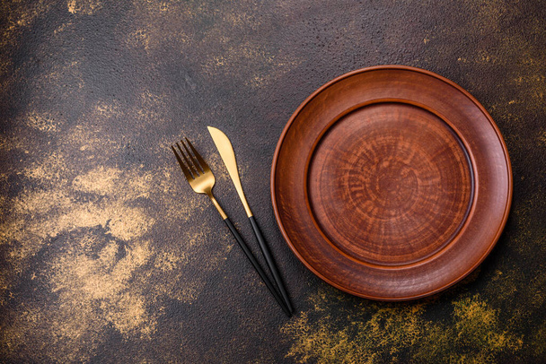 Порожня коричнева керамічна тарілка на темному бетонному коричневому фоні. Готуємо обідній стіл
 - Фото, зображення