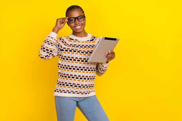 Photo of young confidence girl with cornrows dressed print jumper holding tablet glasses isolated on shine yellow color background. - Foto, immagini