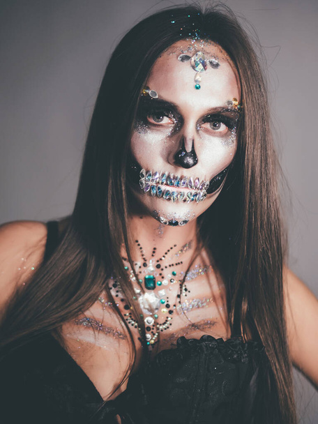 Scary glamour skull sexy woman with creative halloween war-paint. Portrait of glamorous skeleton with rhinestones and sequins. Professional make-up for party celebration. High quality photo - Foto, imagen