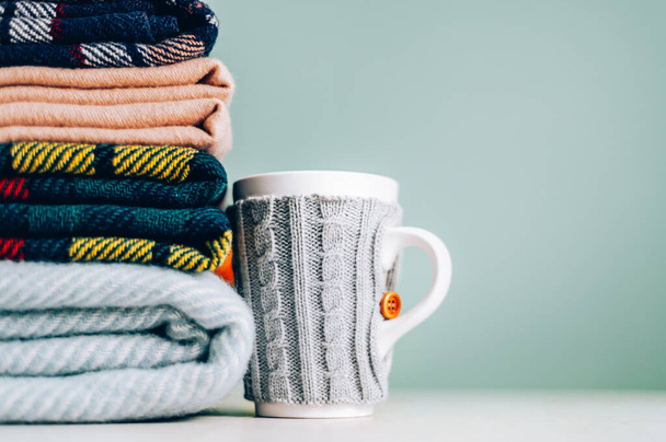 Stack of folded woolen checked blankets and mug in wollen cover, autumn and cold winter concept - Foto, imagen