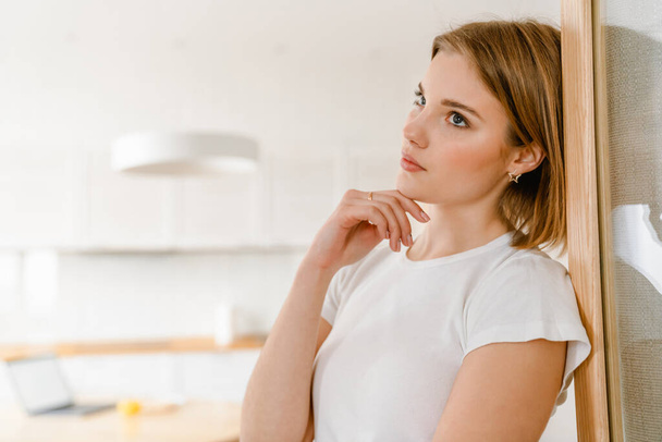 Pensive young woman leaning on a wall in the kitchen at home - Foto, imagen