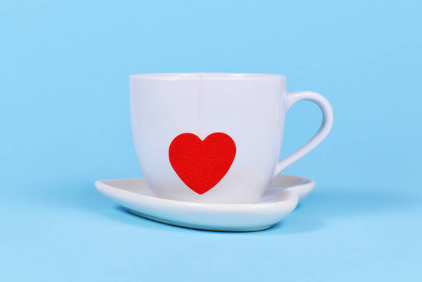 White tea cup with red heart shaped tea bag paper on blue background - Fotó, kép
