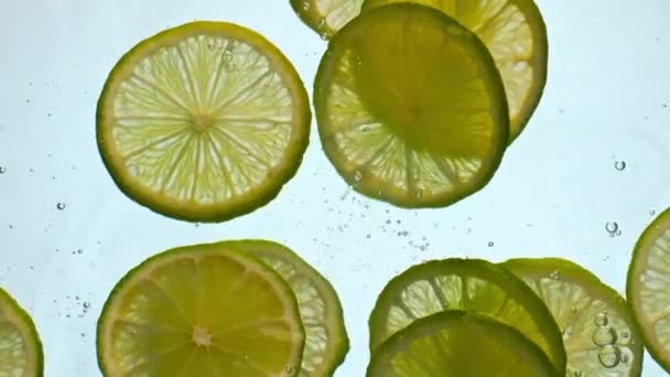 Closeup sliced bright lime floating clear water in super slow motion. Tasty vitamin citrus dropped in transparent liquid for healthy delicious drink. Fresh yellow fruits underwater on white background - Footage, Video